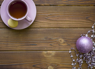 A tea cup with saucer and purple shiny christmas ball on a ructic wooden table, top view