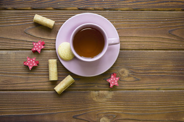 A pink tea cup with saucer, cookies and red stars on a rustoc wooden table, top view