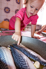 Little girl at the table in the kitchen with fish on the table