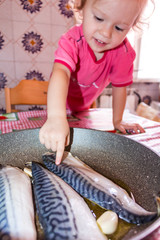 Little girl at the table in the kitchen with fish on the table