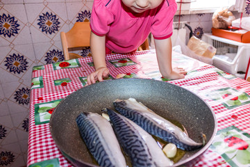 Little girl at the table in the kitchen with fish on the table