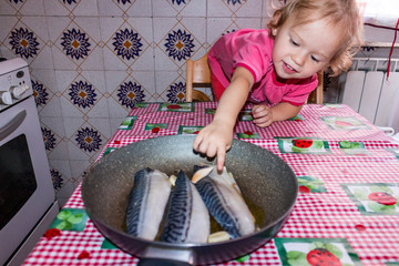 Little girl at the table in the kitchen with fish on the table
