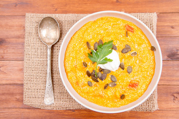 Pumpkin and carrot soup decorated with cream, parsley and pumpkin seeds on a wooden background