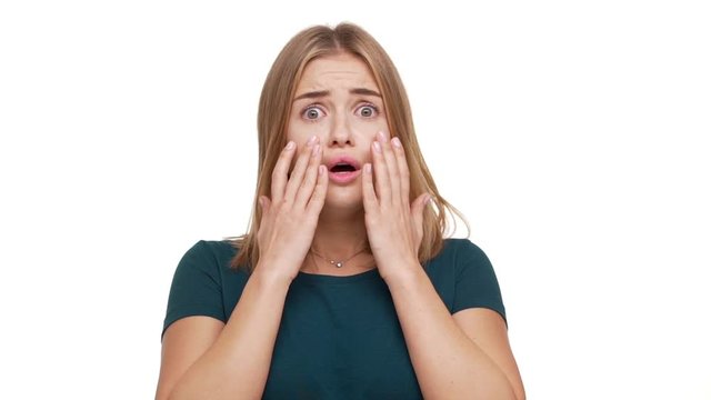 Closeup portrait of young scared woman 20s expressing fright being shocked hearing bad news raising hands to cheeks in fear over white background in slow motion. Concept of emotions