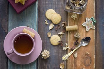 Christmas still life with tea, spoon, cookies, a jar of dry flowers and a purple gift box on a colored wooden background, top view
