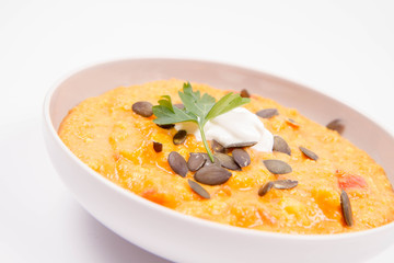 Pumpkin and carrot soup decorated with cream, parsley and pumpkin seeds on a white background