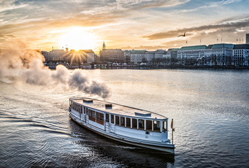 steamboat on Alster Lake in Hamburg, Germany with cityscape in background during sunset - obrazy, fototapety, plakaty