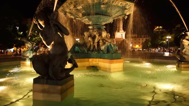 A vivid night shot of the illuminated water fountains with mermaid status in Praca D. Pedro IV, Rossio, Lisboa, Portugal.