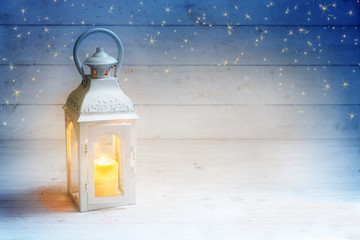 Christmas background with a lantern and burning candle light on rustic white wood, blue sky with...