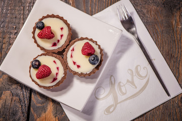 chocolate cupcakes with white cream and red hearts decorated with raspberry and blueberry