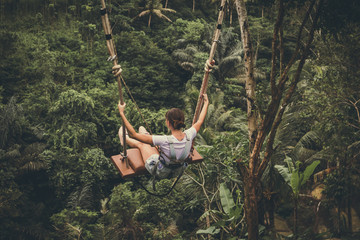 Young tourist woman swinging on the cliff in the jungle rainforest of a tropical Bali island.