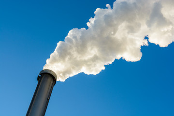 A metallic chimney spitting out a heavy cloud of white smoke against a deep blue sky.