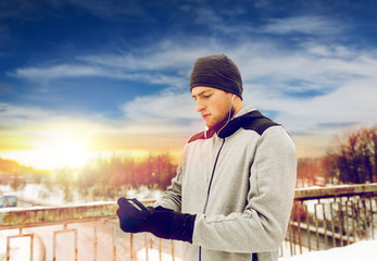 man in earphones with smartphone on winter bridge