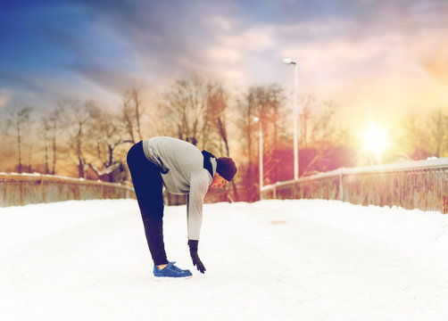 man exercising and stretching leg on winter bridge
