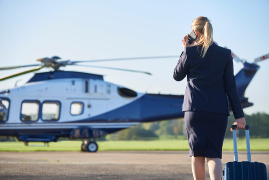 Rear View Of Businesswoman Walking Towards Helicopter Whilst Talking On Mobile Phone