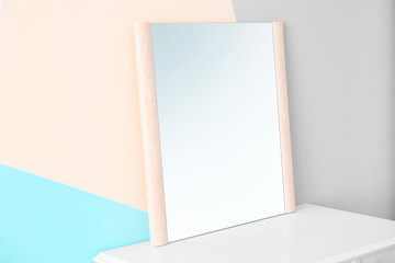 Modern mirror on table near color wall