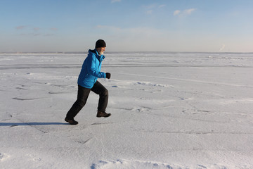 Man in a blue jacket running across the ice of a frozen river, Ob Reservoir, Russia