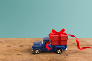 Red Gift box carry on toy car on rustic wood on pastel background. Valentine day, Christmas celebration holiday concept. Use for your design or greeting card.