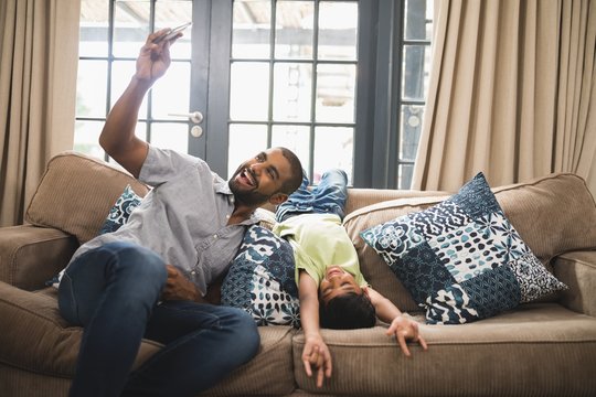 Cheerful man taking selfie with his son on couch at home