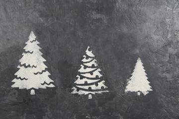 A trace from a stencil in the form of three Christmas trees made of flour on a gray concrete...