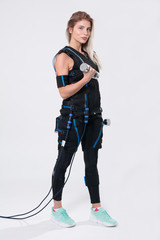 Beautiful blonde in electric muscular suit for stimulation with dumbbells
