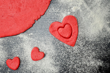 Red dough with cut-out hearts and flour on the black table. top view, close up