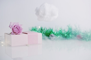 Pink present box with rose on it and cloud with christmas tree decoration on the background. New year minimal concept.