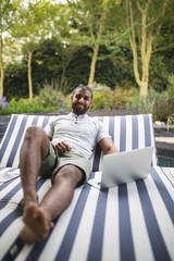 Fototapeta premium Smiling man using laptop while relaxing on lounge chair at porch