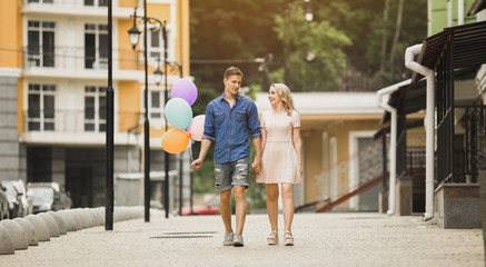 Fototapeta na wymiar Male with balloons and female strolling down street and talking, romantic date
