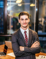 Fototapeta premium Portrait of young businessman smiling working on modern loft office at night sitting at office with team staff and working late overtime.