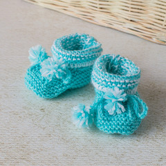 Needlework knitting. Knitted booties for a toddler made of soft fluffy yarn of blue color on a light background.