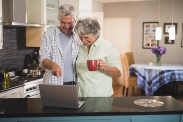 Smiling senior couple watching laptop while standing in kitchen