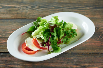 Close up horizontal shot of a plate with caprese Italian traditional salad on a wooden table at the restaurant tomatoes mozarella rucola greend delicious vegan healthy vegetables.