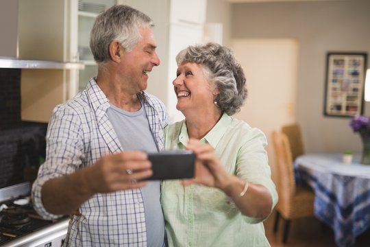 Cheerful Senior Couple With Mobile Phone In Kitchen