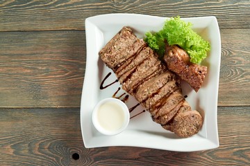 Top view horizontal shot of sliced meat on a white square plate on the wooden table copyspace eating food recipe dinner meal lunch supper roasted sauce greens decorated.