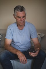 Fototapeta premium Upset senior man holding mobile phone while sitting on sofa