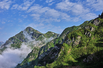 Fototapeta na wymiar Panorama of the mountains in the area of Krasnaya Polyana/Panorama of Sochi in the Krasnaya Polyana area. There are mountains, clouds, air haze, vegetation. Sochi, Russia, mountain landscape 