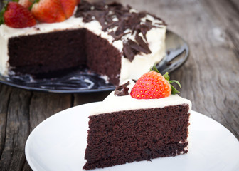 Chocolate cake decorate with whipping cream, sliced chocolate and fresh strawberries. On black plate. Sweet dessert for celebrate.