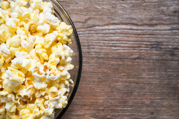 Closeup popcorn in glass bowl. Served on wooden table. Top view with copy space.