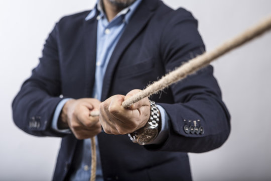 Dettaglio mani di un Manager con giacca e camicia  che tirano una corda  tesa in segno di sfida e forza -  sfondo bianco