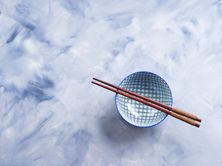 Japanese rice bowl and chopsticks on blue background
