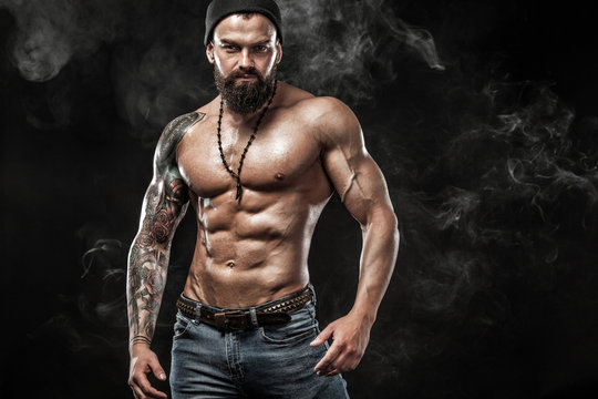 Handsome fit man posing wearing in jeans with tattoo. Sport and fashion concept isolated on black background.