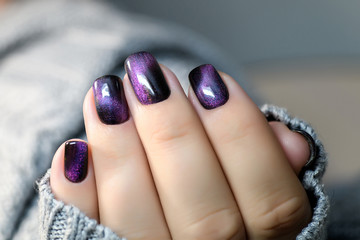 Beautiful nail polish in hand, purple nail art manicure, gray background
