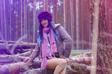 Modern american style woman in faux fur hat and  jacket sit at forest. Young woman with long color mix hair and bright holiday make up on a sawmill