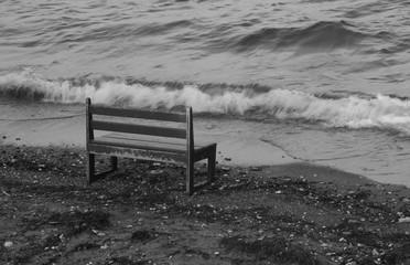 An empty bench seat on beach across waves
