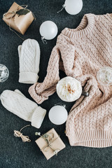 Feminine winter clothes look on grey plaid. Warm beige sweater and white knitted mittens, gift box and glass balls. Christmas fashion composition. Flat lay, top view.