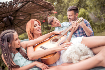 Happy family having fun in the park, playing the guitar.