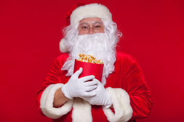 Traditional Santa Claus watching TV, eating popcorn. Christmas. Red background. emotions fear surprise