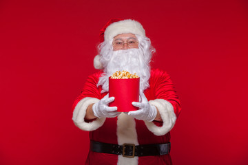 Traditional Santa Claus watching TV, eating popcorn. Christmas. Red background. emotions fear surprise