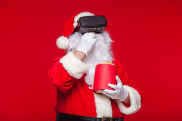 Santa Claus wearing virtual reality goggles and a red bucket with popcorn, on a red background. Christmas